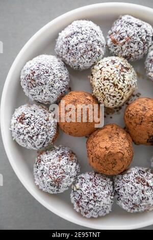 Boules de neige à la noix de coco faites à la main à partir de dattes, truffes aux amandes et à la noix de coco sur une surface grise Banque D'Images