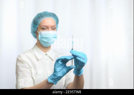 Une infirmière floue portant un masque et des gants bleus en nitrile tient une seringue avec un vaccin. Mise au point sélective. Concept de vaccination contre le coronavirus. Banque D'Images