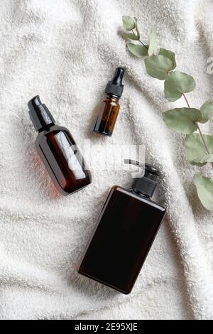 Ensemble de bouteilles cosmétiques en verre ambré et feuille d'eucalyptus sur serviette blanche. SALLE de bains SPA cosmétiques naturels. Flat lay, vue de dessus Banque D'Images