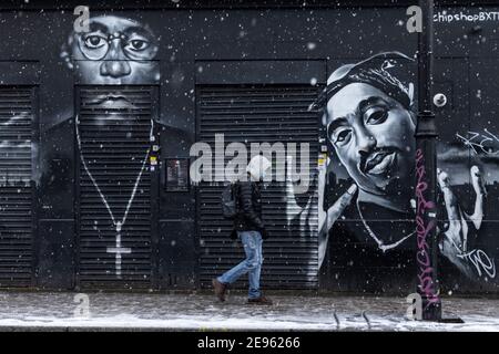 Un homme en masque facial passe devant les peintures murales des rappeurs 'Big l' et '2Pac' pendant la neige épaisse, Atlantic Road, Brixton, Londres, 24 janvier 2021 Banque D'Images