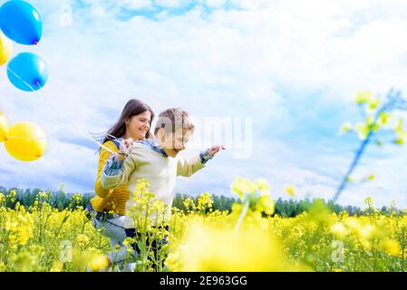 Jeune fille et garçon de 7 ans avec des ballons à l'extérieur.courir le long du champ jaune. Fleur de colza, concept de liberté.magnifique anniversaire d'été Banque D'Images