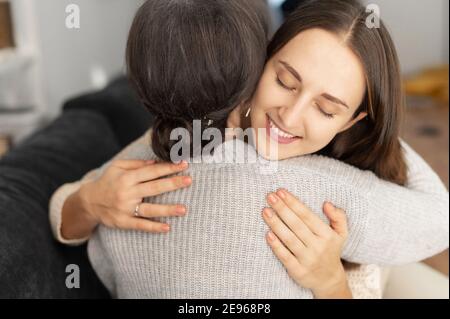 Une fille adulte embrassant une mère aînée assise sur le canapé dans le salon confortable, deux générations différentes femmes embrassant à l'intérieur. Liens familiaux Banque D'Images