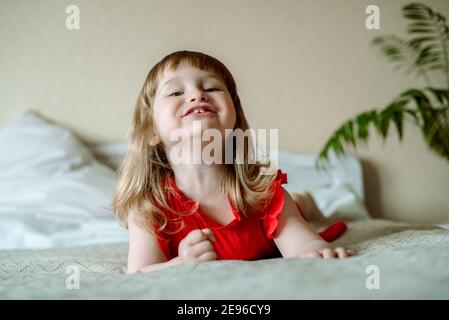 portrait de bébé heureux.emotive bébé fille sur le lit dans une chambre lumineuse. chambre blanche confortable, enfant gai. hurle émotionnellement, rires et réjouissances Banque D'Images