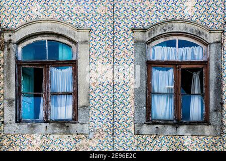 Gros plan de la façade traditionnelle portugaise de maison décorée par de beaux carreaux azulejo en céramique, deux vieilles fenêtres avec des rideaux bleus Banque D'Images