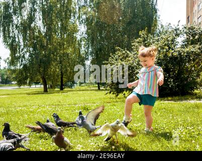 Un enfant nourrit des pigeons dans le parc de la ville en plein air.petite fille qui court près des colombes. Pourchassant les pigeons, heureux enfant souriant.chaud été ensoleillé Banque D'Images