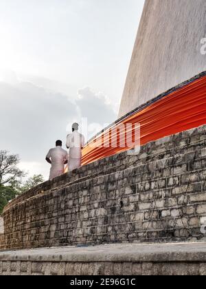 ANURADHAPURA, SRI LANKA - 9 mars 2019 : deux hommes prient sur le temple Ruwanwelisaya dans la ville sacrée Anuradhapura. Tir vertical. Banque D'Images
