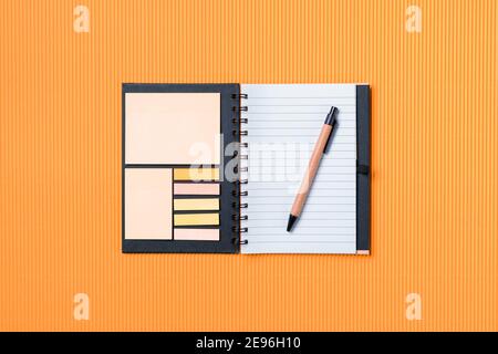 Carnet scolaire sur fond de papier orange, bloc-notes en spirale et stylo de carton artisanal Banque D'Images
