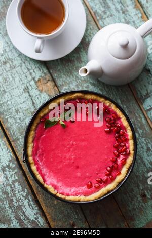 Dessert rose. Tarte aux baies maison aux graines de grenade et à la menthe servie avec du thé noir sur fond bleu de vieux sorbby vue du dessus Banque D'Images