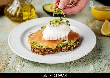 Toast maison avec purée d'avocat, saumon, œuf poché et microverts Banque D'Images