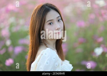 Belle jeune femme avec robe blanche sur fleurs rose cosmos arrière-plan Banque D'Images