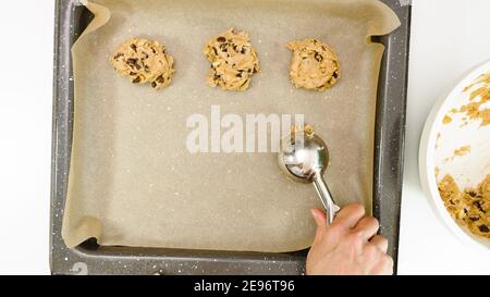 Recette de biscuits aux pépites de chocolat. Femme plaçant la pâte à biscuits sur une plaque de cuisson, gros plan, vue d'en haut Banque D'Images