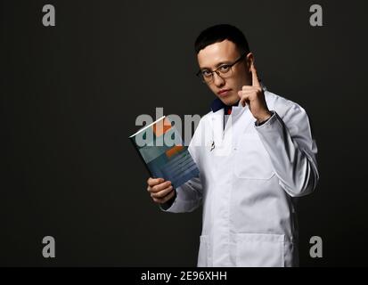 Jeune homme médecins en blanc uniforme médical robes tient livres professionnels avec couverture vierge à la main et doigt vers le haut Banque D'Images