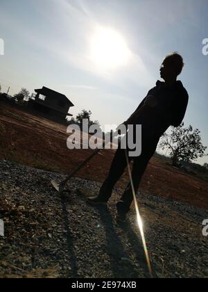 Silhouette d'un vieil homme tenant une houe sur le terrain vacant avant la culture. Banque D'Images