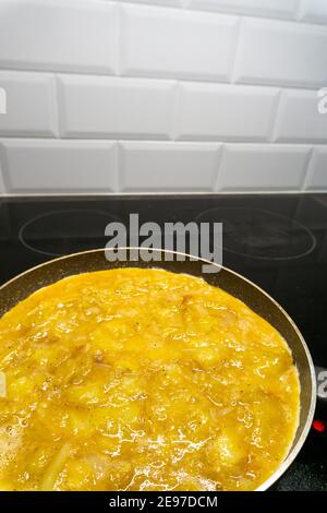 Vue sur une omelette aux pommes de terre avec oignon et poivre en préparation dans une casserole, dans une cuisine avec une plaque vitrocéramique Banque D'Images