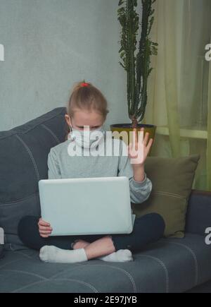 fille d'école masquée regarde des leçons vidéo sur ordinateur portable en quarantaine Banque D'Images