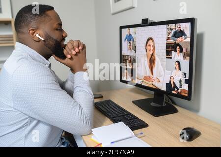 Vue sur l'épaule d'un homme africain à l'aide d'un ordinateur. L'écran du PC permet d'afficher des personnes diverses qui discutent via des appels vidéo à distance. Application pour la communication à distance avec Banque D'Images