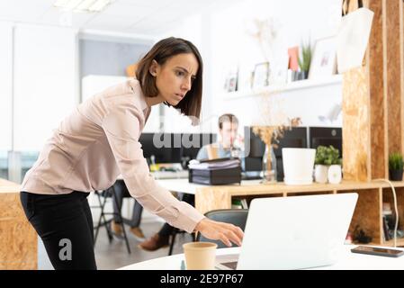 Une femme hispanique sérieuse espionne l'ordinateur portable de son collègue au bureau. Banque D'Images
