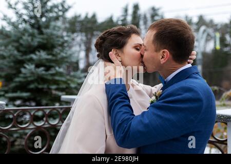 deux jeunes mariés lors d'une promenade de mariage en hiver, les amoureux se bernent et embrassent doucement, deux adultes à une date Banque D'Images