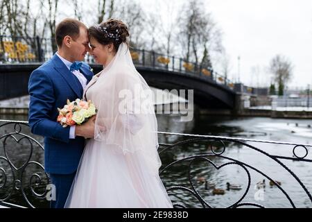 deux jeunes mariés lors d'une promenade de mariage en hiver, les amoureux se bernent et embrassent doucement, deux adultes à une date Banque D'Images