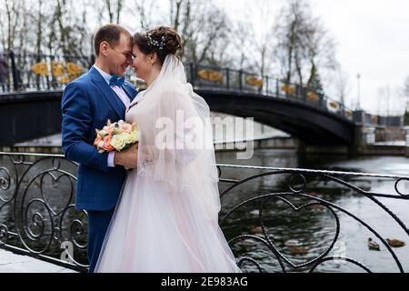 deux jeunes mariés lors d'une promenade de mariage en hiver, les amoureux se bernent et embrassent doucement, deux adultes à une date Banque D'Images