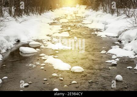 Paysage d'hiver de rivière étroite de montagne peu profonde qui coule dans la neige forêt au coucher du soleil Banque D'Images
