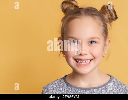 L'enfant montre ses dents saines. Gros plan sur le visage d'une petite fille mignonne qui sourit en montrant des dents sur un fond jaune. Art dentaire pédiatrique con Banque D'Images