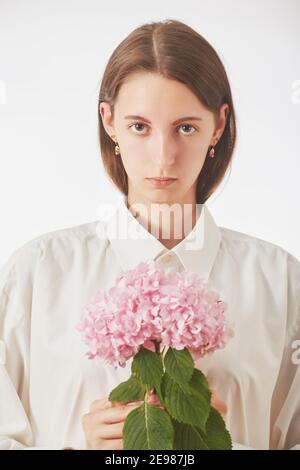 jeune femme sérieuse avec fleur rose sur fond blanc, regardant l'appareil photo Banque D'Images