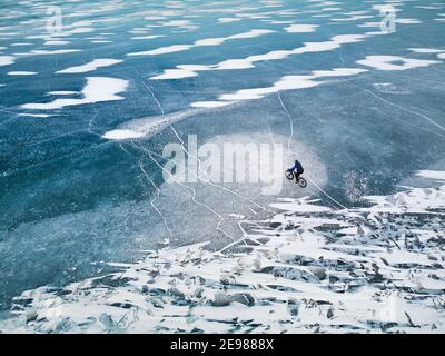 Vue de dessus un tir de drone d'homme à vélo sur le lac gelé avec texture de glace. Banque D'Images