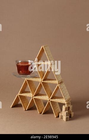 Encore une vie de composition créative avec biscuit et tasse de thé équilibré dans une forme de triangle avec des morceaux de sucre brun. Banque D'Images