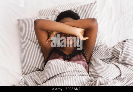 Une jeune femme sans sommeil souffrant d'insomnie, couchée au lit, couvrant les yeux avec les mains, essayant de dormir Banque D'Images
