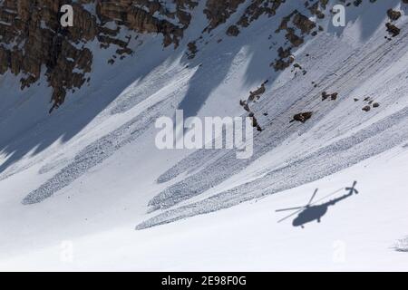 Ombre d'un hélicoptère sur une pente enneigée hors-piste avec des traces d'avalanches par beau temps d'hiver. Hélicoptère de sauvetage dans les hautes montagnes. Banque D'Images