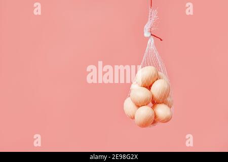 les œufs de poulet dans le filet du sac sont suspendus sur fond rose Banque D'Images