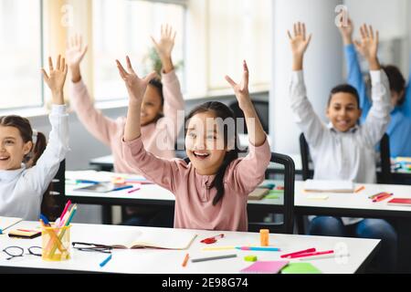 Heureux divers petits écoliers levant les mains en classe Banque D'Images