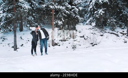 Joyeux jeune couple embrassant entouré d'une forêt à feuilles persistantes recouverte de neige. Esprit de Noël. Photo de haute qualité Banque D'Images