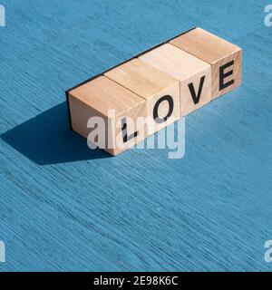 Concept de la journée et des sentiments de Valentin : le mot AMOUR écrit avec des lettres cubes en bois simples faites pour les jeux de société sur une surface texturée bleue avec espace Banque D'Images