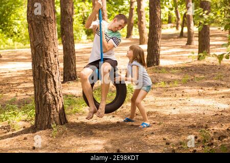 Enfant heureux fille poussant le père sur le balancement de pneu dans le jardin d'automne. Photo de haute qualité Banque D'Images