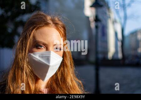 Bonne jeune femme avec de beaux yeux bleus et des cheveux de gingembre Port d'un masque facial (FFP-2) pour la protection contre les virus pendant le Pandémie COVD-19 Banque D'Images