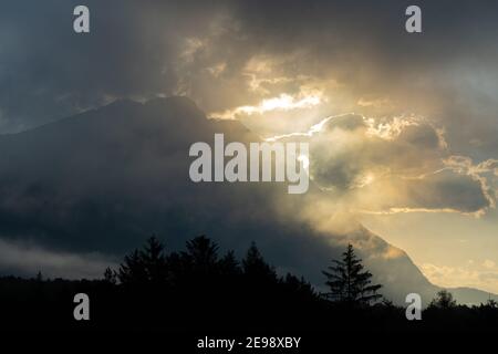 Soleil sortant derrière les nuages au-dessus des arbres Banque D'Images