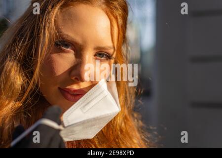 Bonne jeune femme avec les yeux bleus et les cheveux de gingembre en retrait Un masque protecteur pour le visage (FFP-2) pendant la pandémie de COVD-19 Banque D'Images