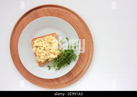 Sandwich à la salade d'œufs avec du pain grillé au blé entier et des micro-légumes sur plaque sur fond blanc. Concept d'alimentation saine Banque D'Images