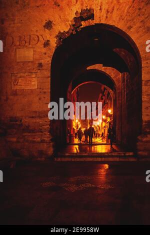 Valence, Espagne - 17 février 2020 : vue à travers l'arche des murs médiévaux du fort « Torres de Quart » sur une rue orange illuminée avec des personnes en mouvement floues Banque D'Images