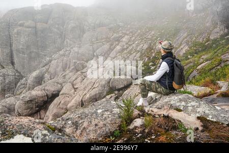 Jeune femme en vêtements de sport assise sur des rochers en admirant le paysage du parc national Andringitra, grand massif de pierres, pendant la randonnée jusqu'à pic Banque D'Images