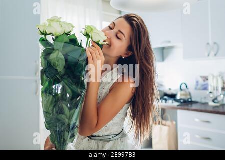 Cadeau de Saint-Valentin. Bonne jeune femme sentant bouquet de roses fleurs du mari sur la cuisine. Journée des femmes. Surprise du petit ami Banque D'Images