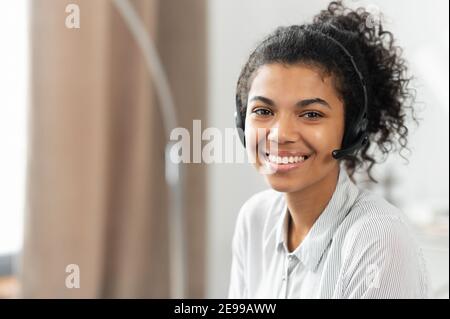 Photo de la charmante femme afro-américaine de race mixte dans le casque, souriant à la caméra travaillant dans le service à la clientèle comme appel Banque D'Images