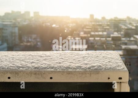 La neige sur une unité de climatisation extérieure fond sous la lumière du soleil pour un paysage urbain flou. Vue depuis la fenêtre du 10e étage. Ressort. Banque D'Images