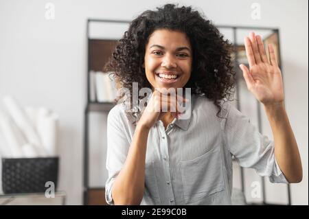 Sympathique adorable afro-américaine femme employée de bureau femme d'affaires freelance avec la coiffure afro joyeusement agitant, souriant et disant salut, faire Banque D'Images