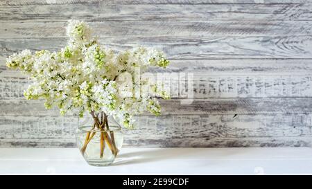 Bouquet de lilas blanc dans un vase en verre sur une table en bois. Branches printanières de lilas fleurs bouquet festif de fleurs. Longue bannière Web avec espace de copie. Banque D'Images