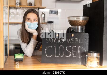 Une femme triste propriétaire de café se sent aspirant en raison de fermé en raison de quarantaine du coronavirus, verrouillage. Une femme en masque médical et des gants lui mettent la tête Banque D'Images