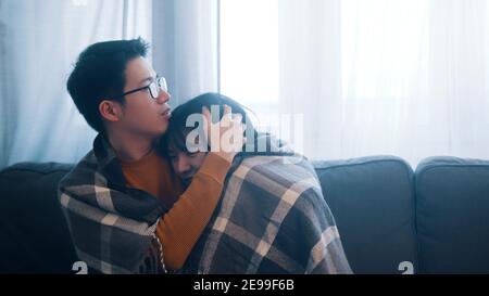 Jeune couple asiatique assis sur le canapé recouvert d'une couverture. Tempête et tonnerre à l'extérieur. Photo de haute qualité Banque D'Images
