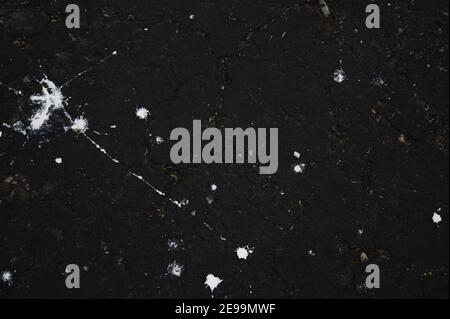 Des projections de peinture blanche renversées font des constellations sur de l'asphalte noir frais. Banque D'Images